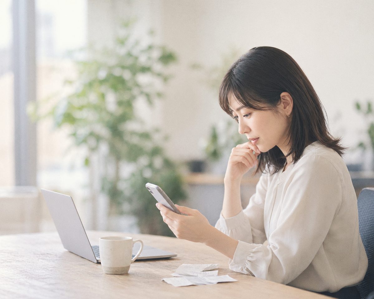 スマートフォンで領収書の内容を確認する、オフィスで働く女性